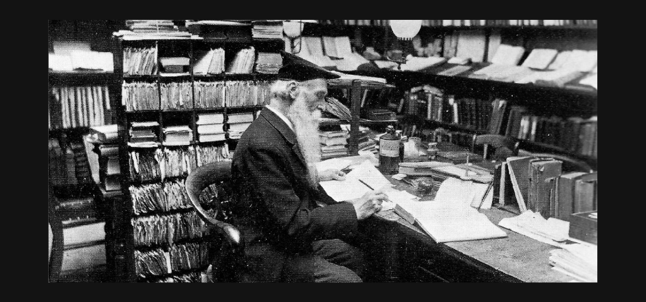 Foto en blanco y negro de un anciano leyendo rodeado de libros en una biblioteca